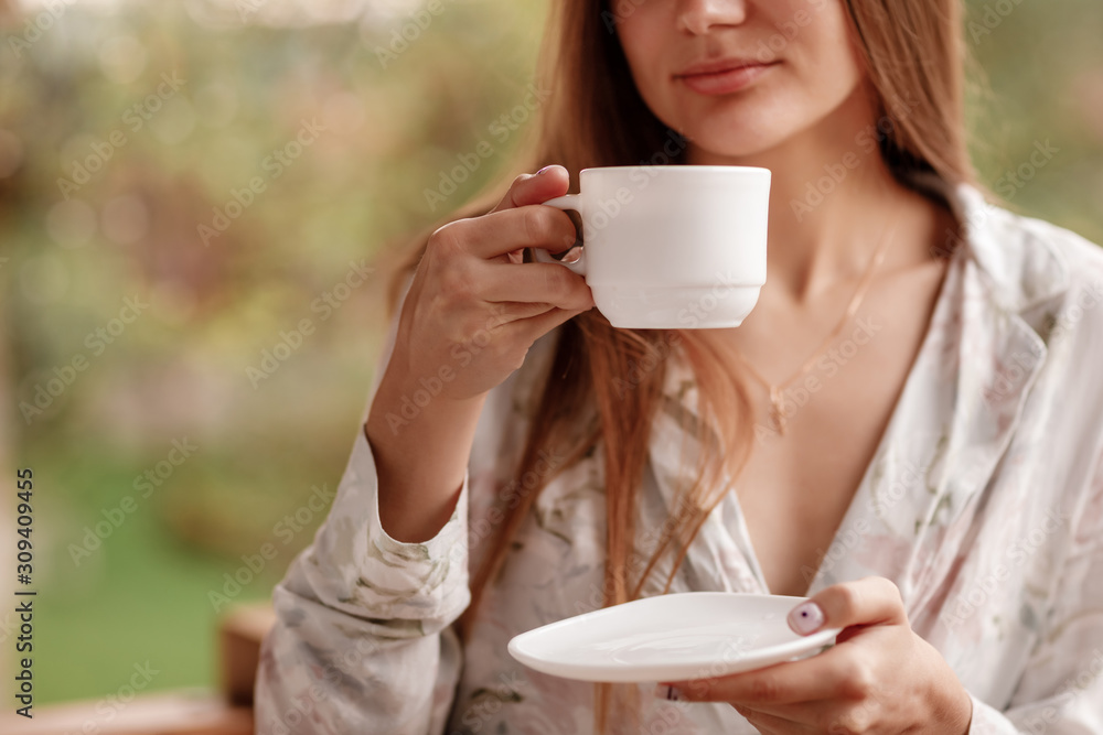 portrait of young woman on the balcony holding a cup of coffee or tea in the morning. She in hotel room looking at the nature in summer. Girl is dressed in stylish nightwear. Relax time portrait of young woman on the balcony holding a cup of coffee or tea in the morning. She in hotel room looking at the nature in summer. Girl is dressed in stylish nightwear. Relax time