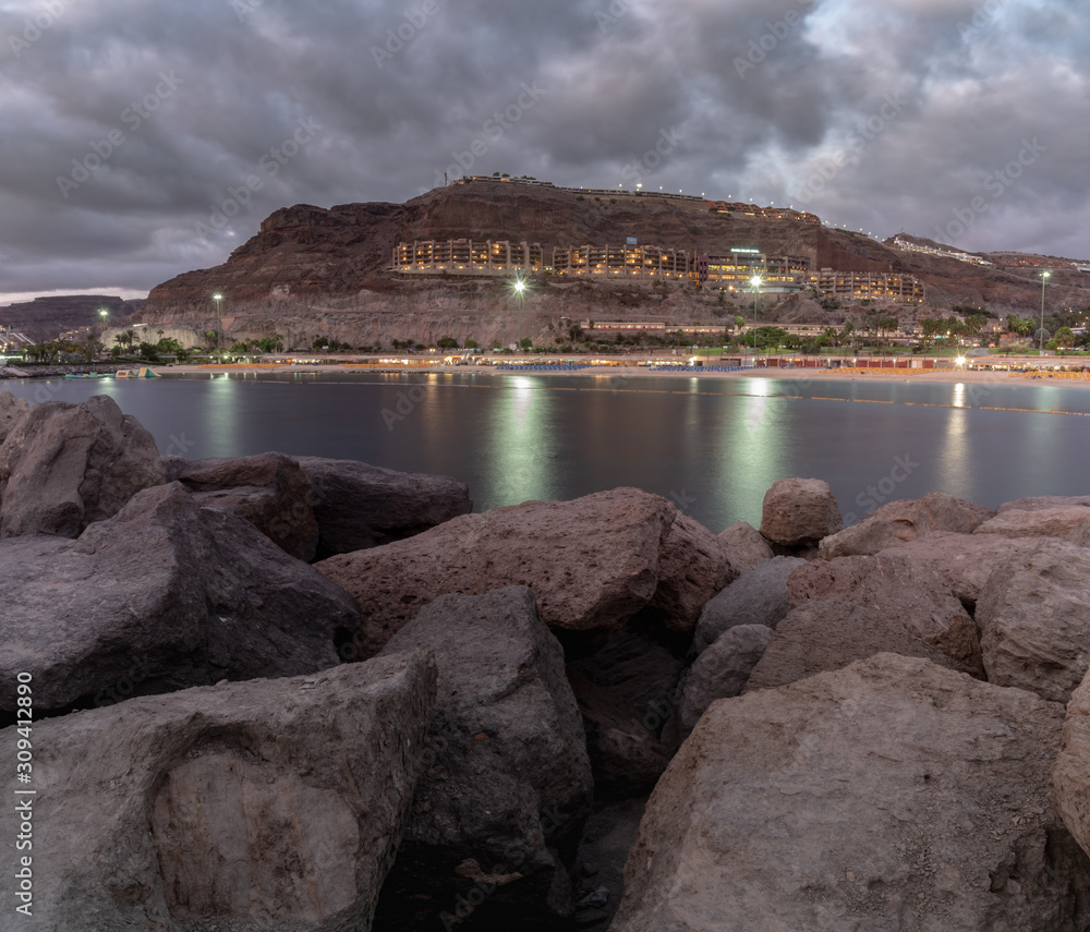 Panoramic view on the bay at night in Puerto Rico, Gran Canaria, Spain. Iluminated buildings in background and silky water with pedalo floating