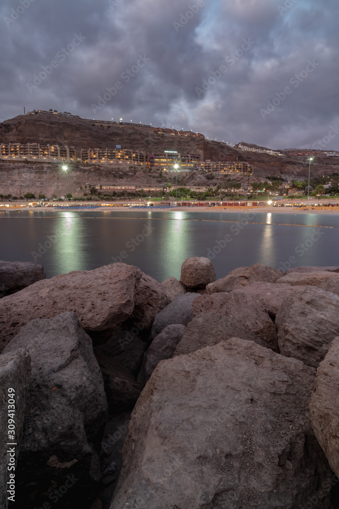 Panoramic view on the bay at night in Puerto Rico, Gran Canaria, Spain. Illuminated buildings in background and silky water with pedalo floating