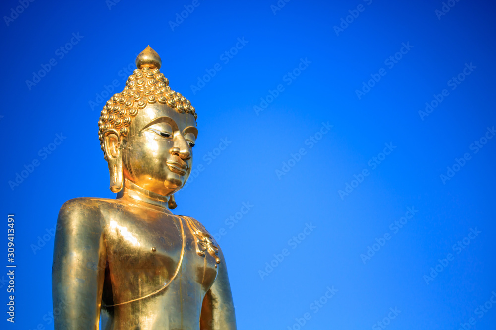 Big golden buddha statue sitting on blue sky background.