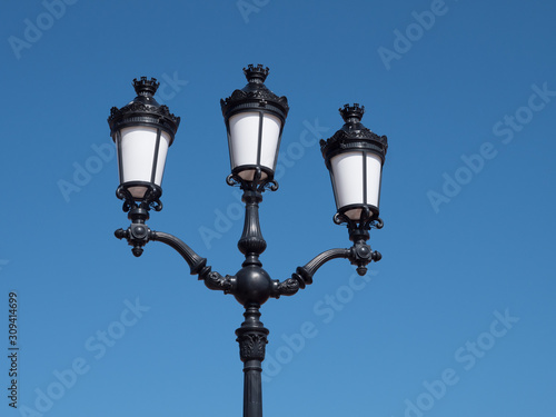 Straßenlaterne mit drei Lampen vor blauem Himmel