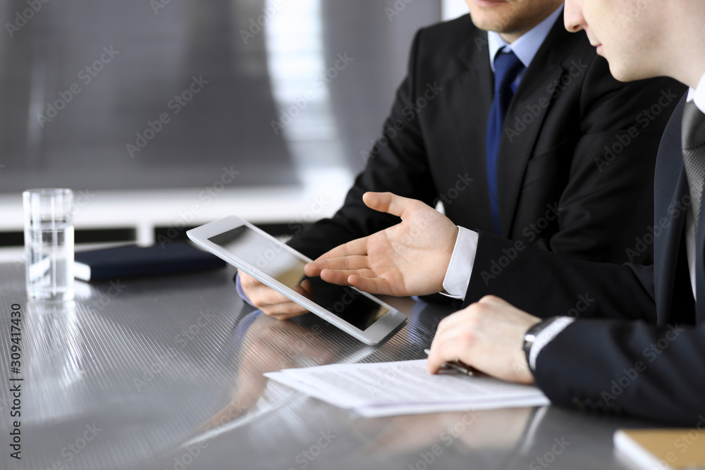 Businessman using tablet computer and work together with his colleague or partner at the glass desk in modern office, close-up. Unknown business people at meeting Businessman using tablet computer and work together with his colleague or partner at the glass desk in modern office, close-up. Unknown business people at meeting