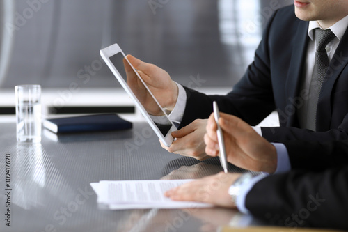 Businessman using tablet computer and work together with his colleague or partner at the glass desk in modern office, close-up. Unknown business people at meeting