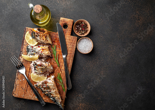 baked mackerel on a cutting board with lemon and spices on a stone background with copy space for your text