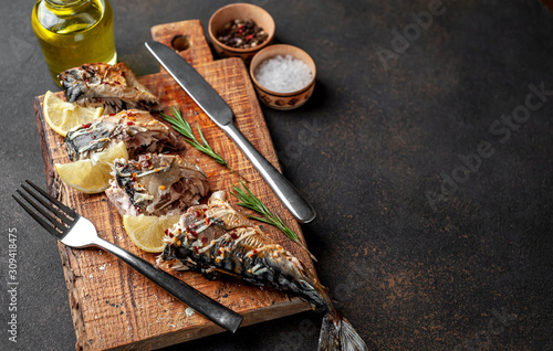 baked mackerel on a cutting board with lemon and spices on a stone background with copy space for your text