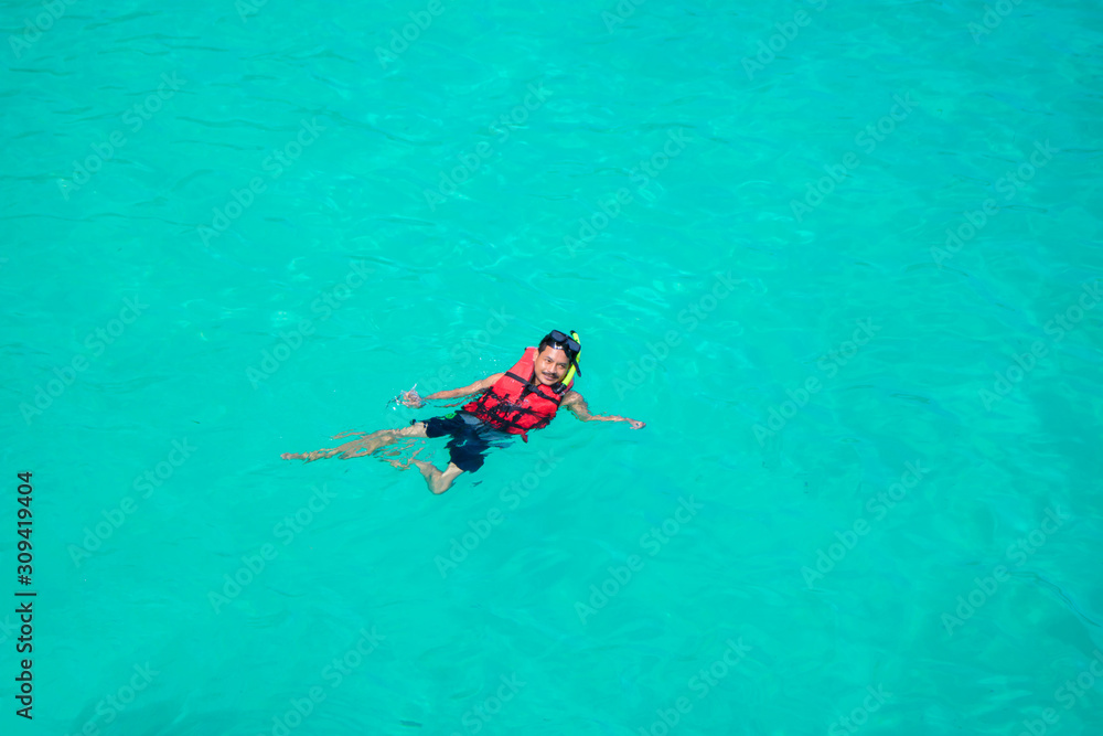 Young man snorkeling in clean water over coral reef.