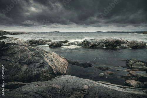 Waves of stormy sea break on rocky shore. Dramatic sky