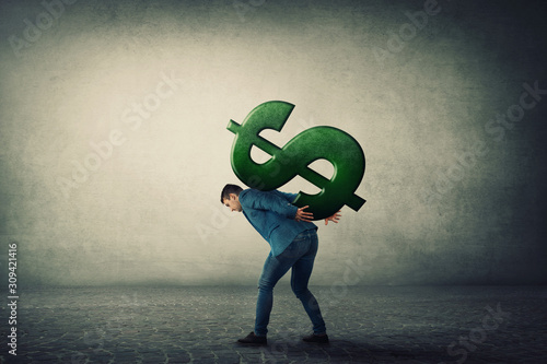 Businessman carrying a big american dollar sign on his back. Overloaded guy, difficult burden and debt pressure. Business corruption issue. Financial crisis concept.