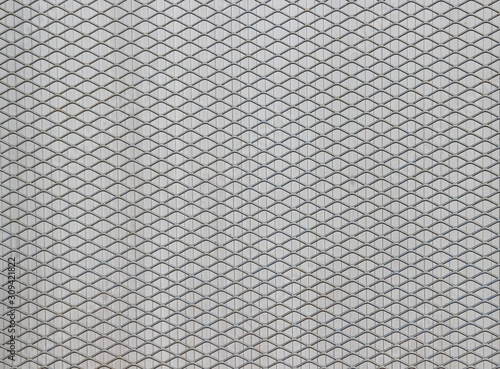 Surface of a latticed metal fence with diamond-shaped elements in front of a wall made of narrow plastic strips