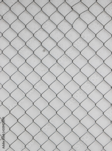 Surface of a wire netting with diamond-shaped elements in front of a white wall 
