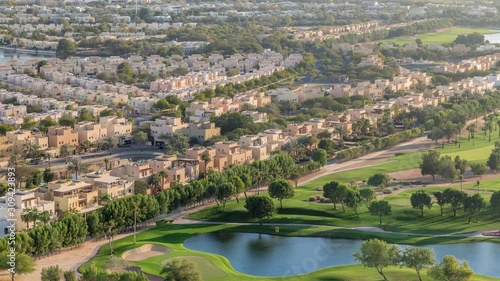 Aerial view to villas and houses with Golf course with green lawn and lakes timelapse. Traffic on streets. Warm evening light photo