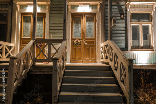Old wooden door in a wooden house with stairs decorated in the evening for Christmas