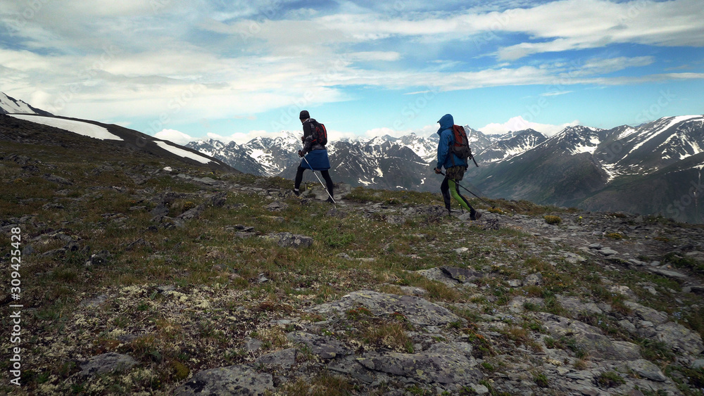 Two tourists walking in the mountains with backpacks and poles. Trekking in the mountains, hills and mountains in sports tourism.