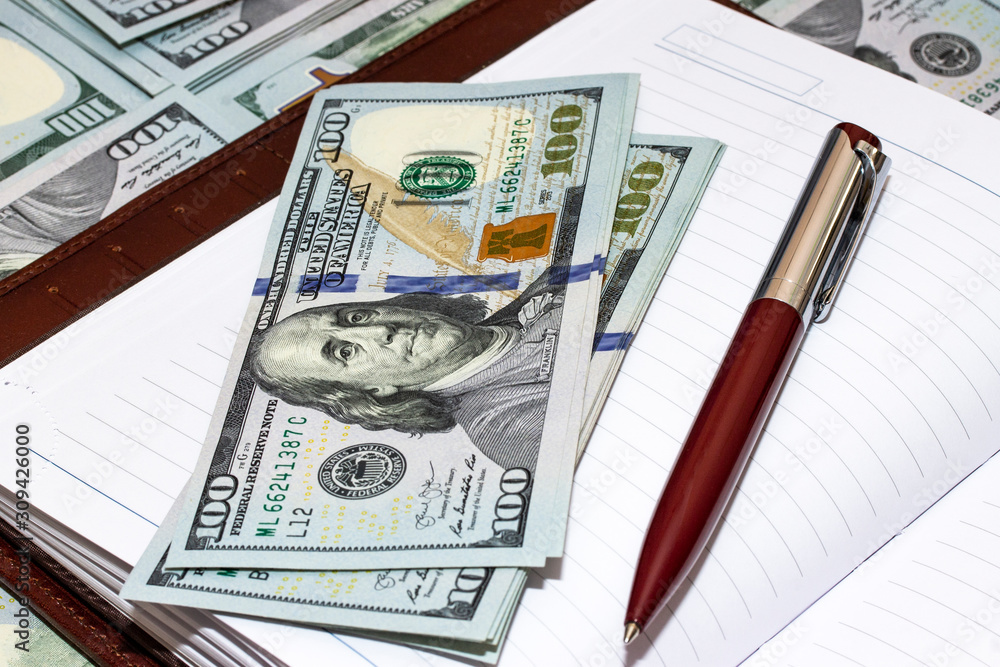 Business notepad and a pen with a pile of US dollars Business notepad and a pen with a pile of US dollars