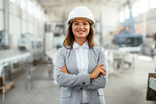 Portrait of businesswoman in factory. Young female architect with helmet in suit.  © JustLife