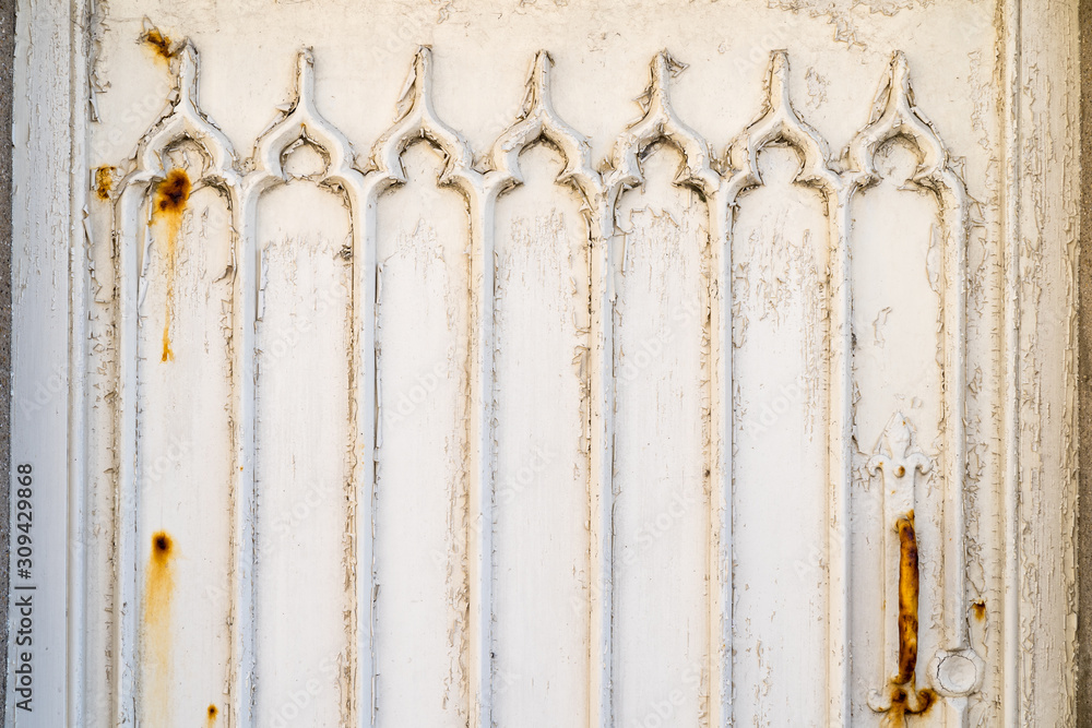 Detail of a white wooden door with weathered and rusty paint and gothic window pattern relief Detail of a white wooden door with weathered and rusty paint and gothic window pattern relief
