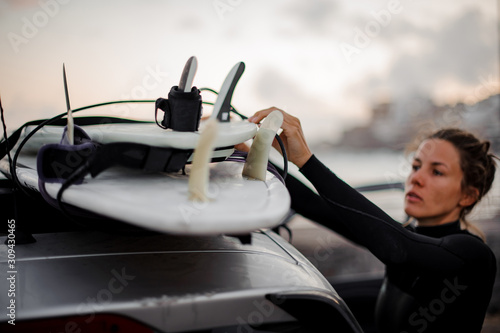 Surfer girl taking surf board from car roof