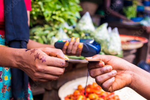 close up of an african woman selling in a local african market holding a mobile point of sale device collecting a credit card from a customer