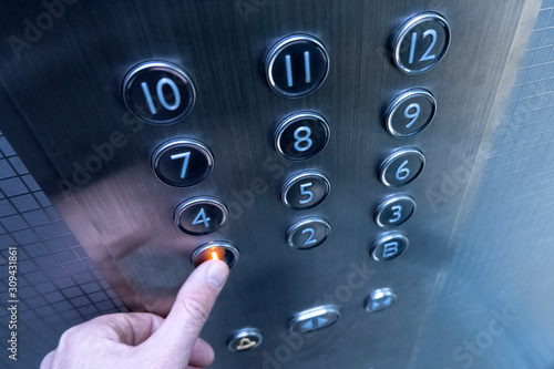 The hand presses on the first floor elevator button. A man in a metal elevator. A twelve-story building. Selective focus. Shallow depth of field. Blurry.