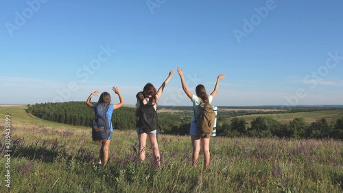 women travelers raise their hands and rejoice. Mom and children are tourists. teamwork travelers. adventure concept. group of tourists travels through flower field and enjoys nature from mountain.