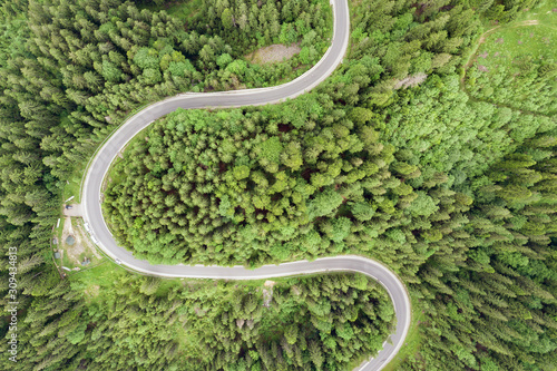 Top down aerial view of winding forest road in green mountain spruce woods.