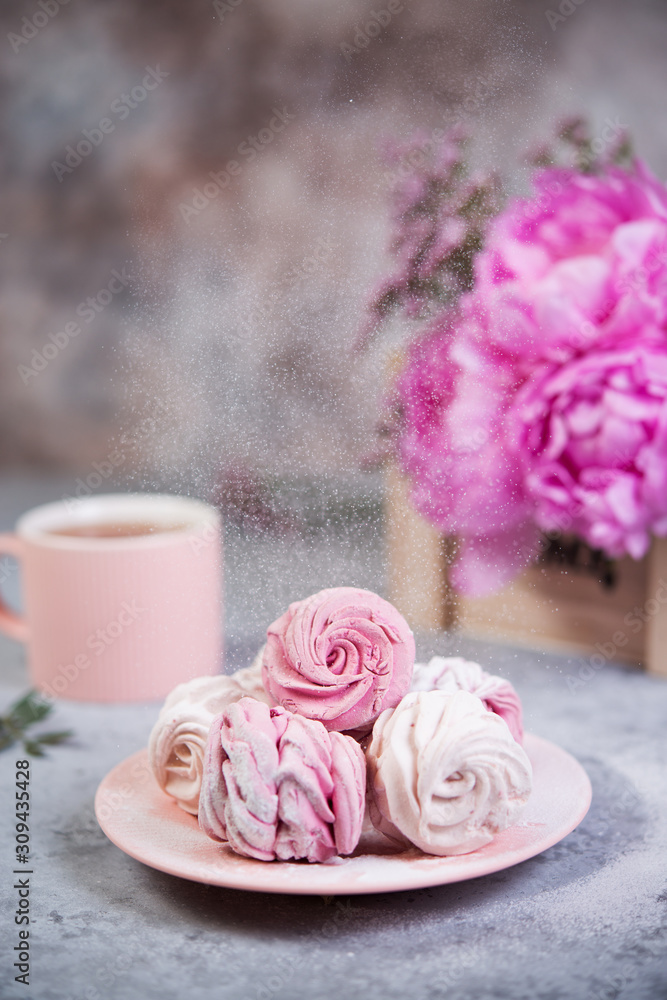 Homemade berry marshmallow in a plate is on the table with a Cup of tea. Powdered sugar falls on top of marshmallows..