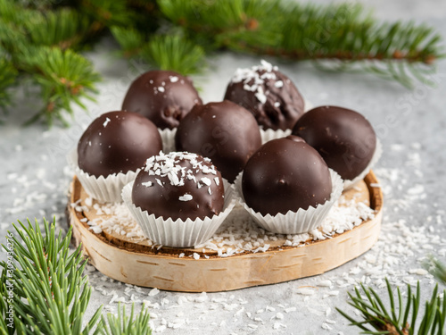 Winter dessert, healthy sugarfree peanut butter truffles covered by dark chocolate and coconut shred, christmas and new year background, fir tree branches, wooden plate, white background