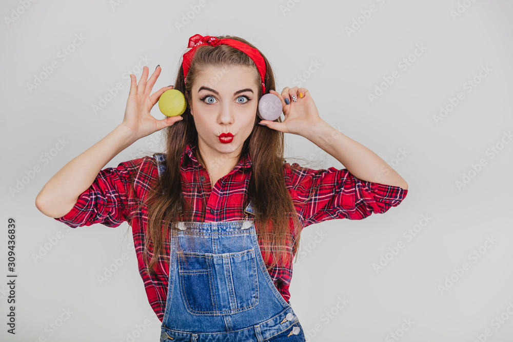 Funny lovely girl is playing around, holding two sweet macaroons near ears, looking like Cheburashka, making faces. Funny lovely girl is playing around, holding two sweet macaroons near ears, looking like Cheburashka, making faces.