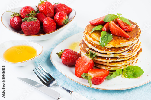 American pancakes lined with strawberries and honey poured on a white background. Classic American Breakfast.
