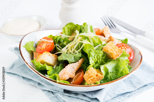 Caesar salad with chicken breast  tomatoes and wheat croutons in a plate on a white background. Horizontal photo.