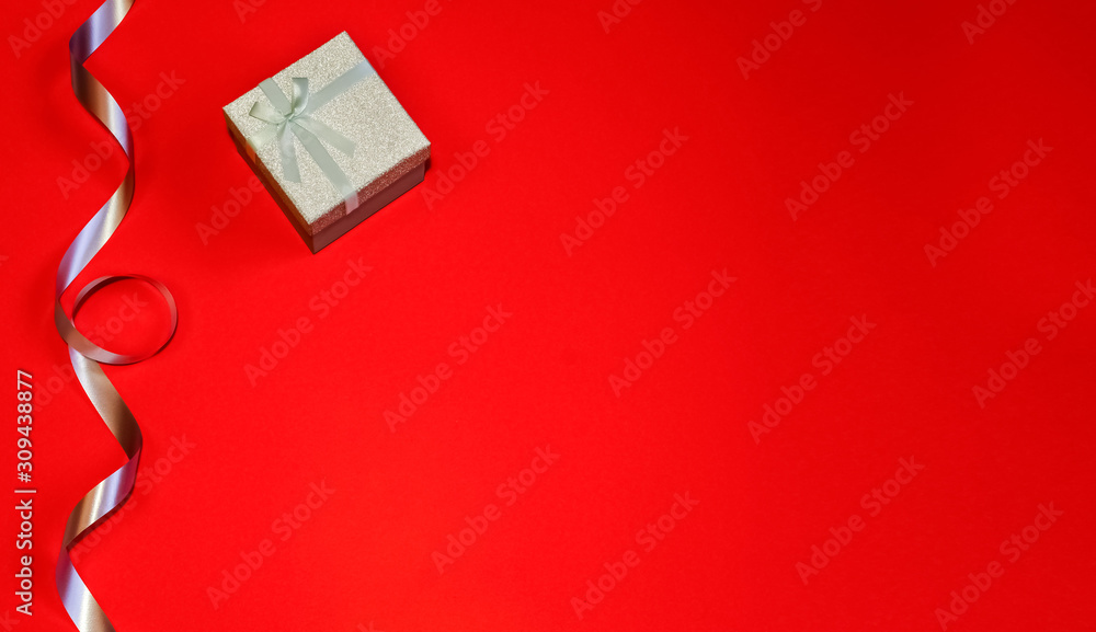 Small gift box with decor of gift blue ribbon on a red background. Space for your text