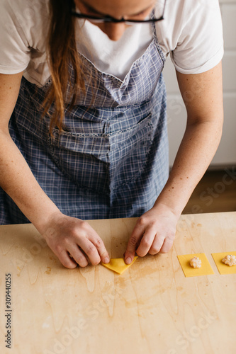 Young woman shaping fresh ravioli on wooden cutting board