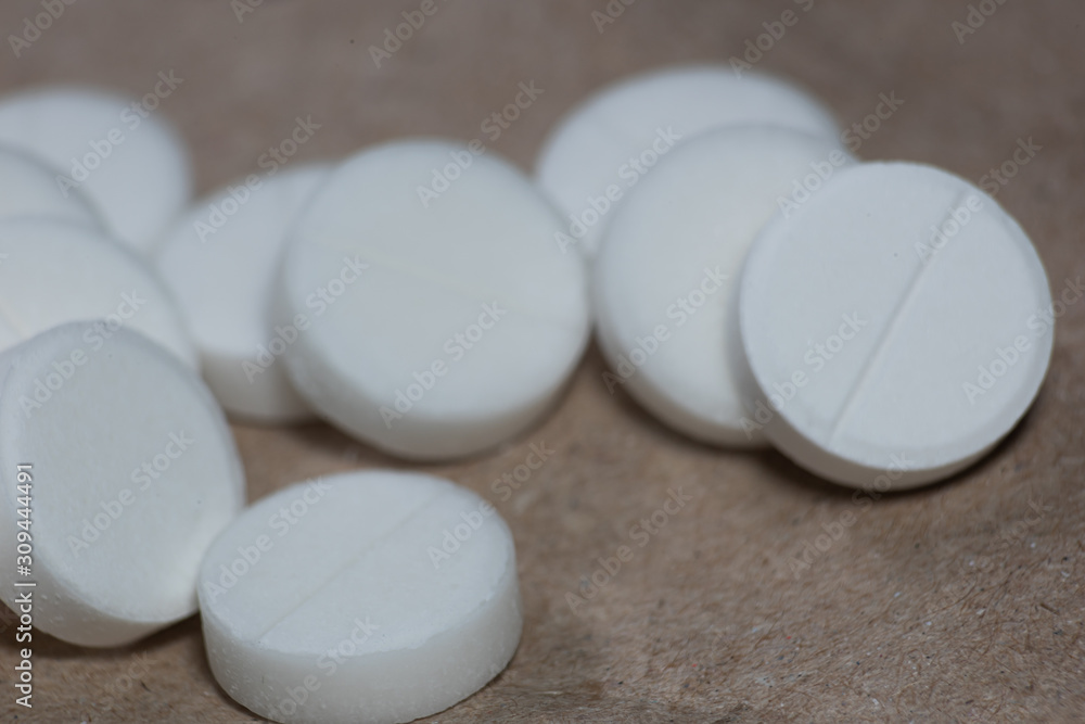 A pile of white pills lie on a craft paper is close A pile of white pills lie on a craft paper is close