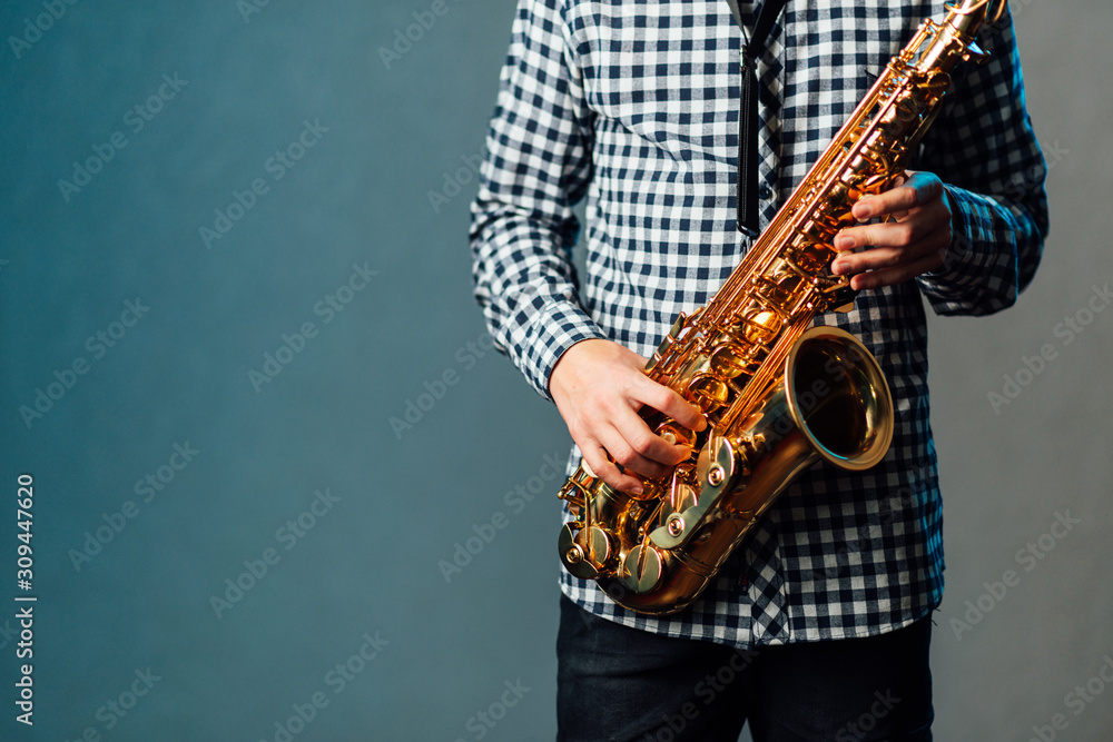 Naklejka premium saxophone in hands close-up on blue uniform background