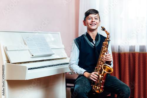 Canvas Print Cheerful student boy sitting with saxophone before music lesson