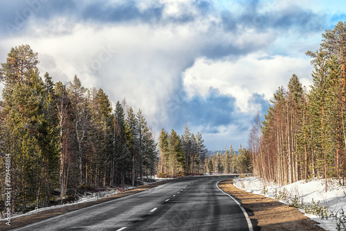 The lonely automobile road in the forest with the dramatic sky