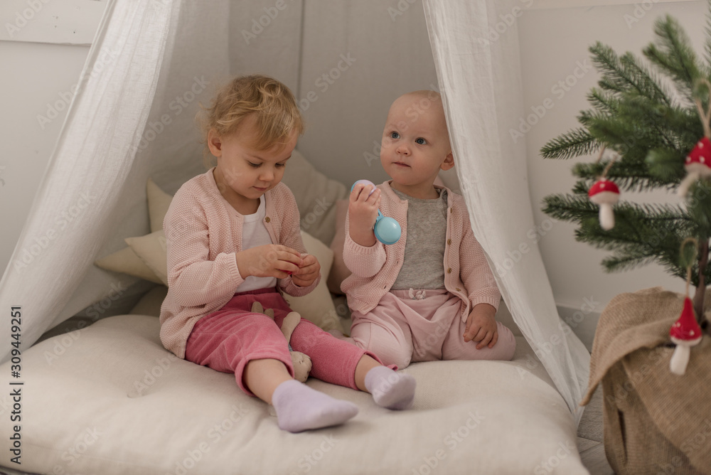Two cute little baby girls play in a spacious bright minimalistic children's room. Two cute little baby girls play in a spacious bright minimalistic children's room.