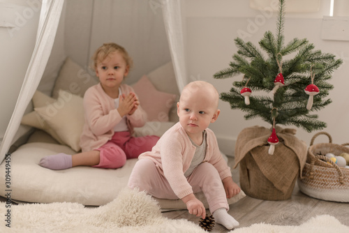 Two cute little baby girls play in a spacious bright minimalistic children's room.