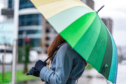 Woman with bright colored rainbow umbrella outdoors. Rain protection on a rainy day and rain weather in the fall