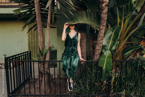 Woman holding a leaf over her face with green hair and green clothes sitting on a fence photo