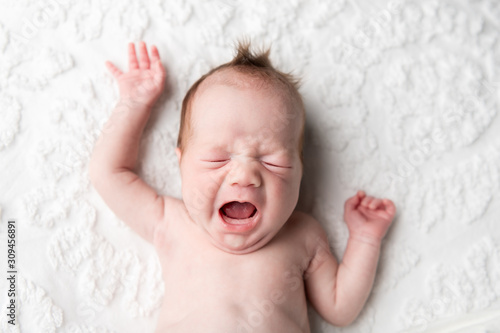 A baby with a big yawn laying on a chenille blanket photo