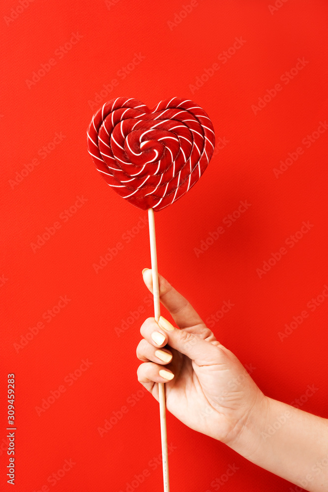 Female hand holding a large red and white striped lollipop. The concept of Valentine's Day, love and friendship. Minimal simple vertical flat lay composition layout. Natural material and light Female hand holding a large red and white striped lollipop. The concept of Valentine's Day, love and friendship. Minimal simple vertical flat lay composition layout. Natural material and light