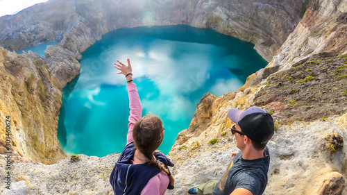Couple standing at the volcano rim and watching the Kelimutu volcanic crater lakes in Moni, Flores, Indonesia. They are having fun, enjoying the view on lake shining with many shades of turquoise photo
