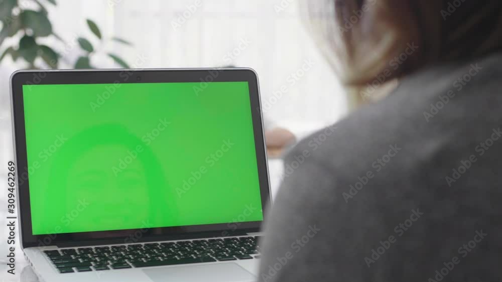 Over the shoulder shot of Asian woman looking at green screen. Office person using laptop computer with laptop green screen, 4K dolly shot Over the shoulder shot of Asian woman looking at green screen. Office person using laptop computer with laptop green screen, 4K dolly shot
