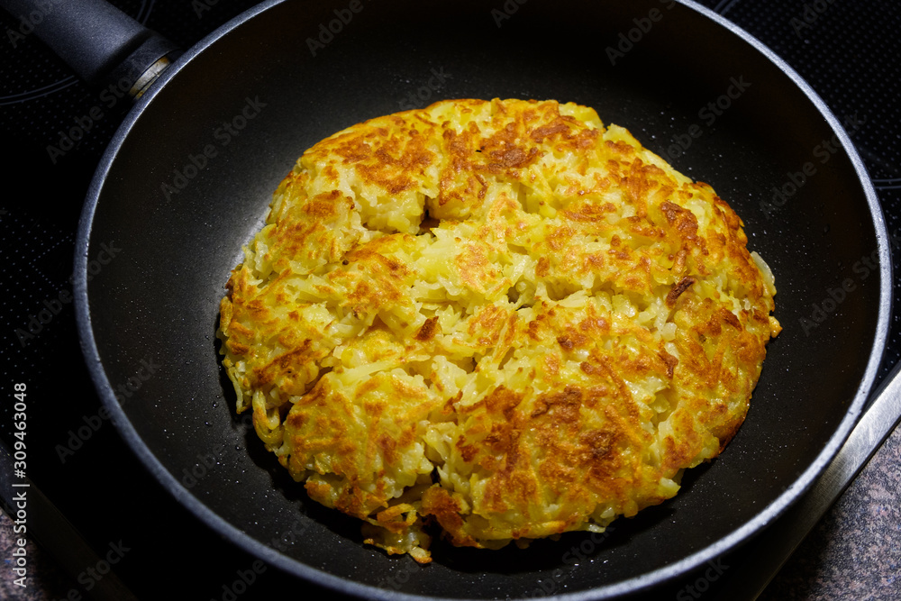 Traditional Swiss roesti (hash browns) closeup in a frying pan, golden roasted potatoes