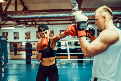 Young woman exercising with trainer at boxing and self defense lesson.