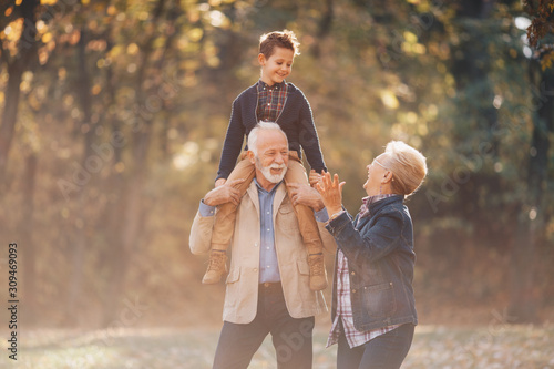 A wonderful day with their grandson. The grandparents are walking with their grandchild on his grandfather's shoulders, and the grandmom walking beside them, both showering the child with love.