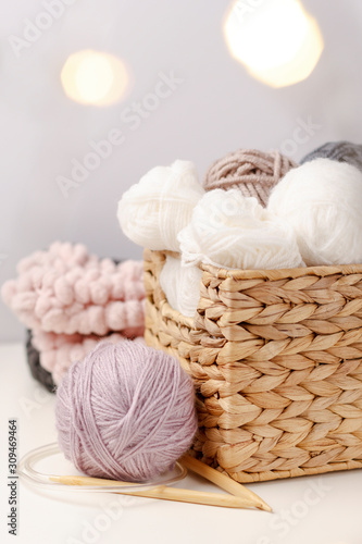 Wooden knitting needles and balls of yarn in wicker basket on light background. Concept of hobby. Handicraft