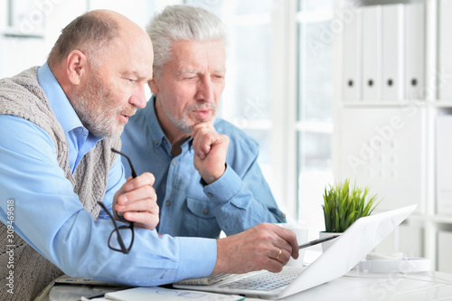 Two senior men sitting at table and using laptop