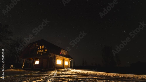 Time lapse of night sky with a log cabin in winter